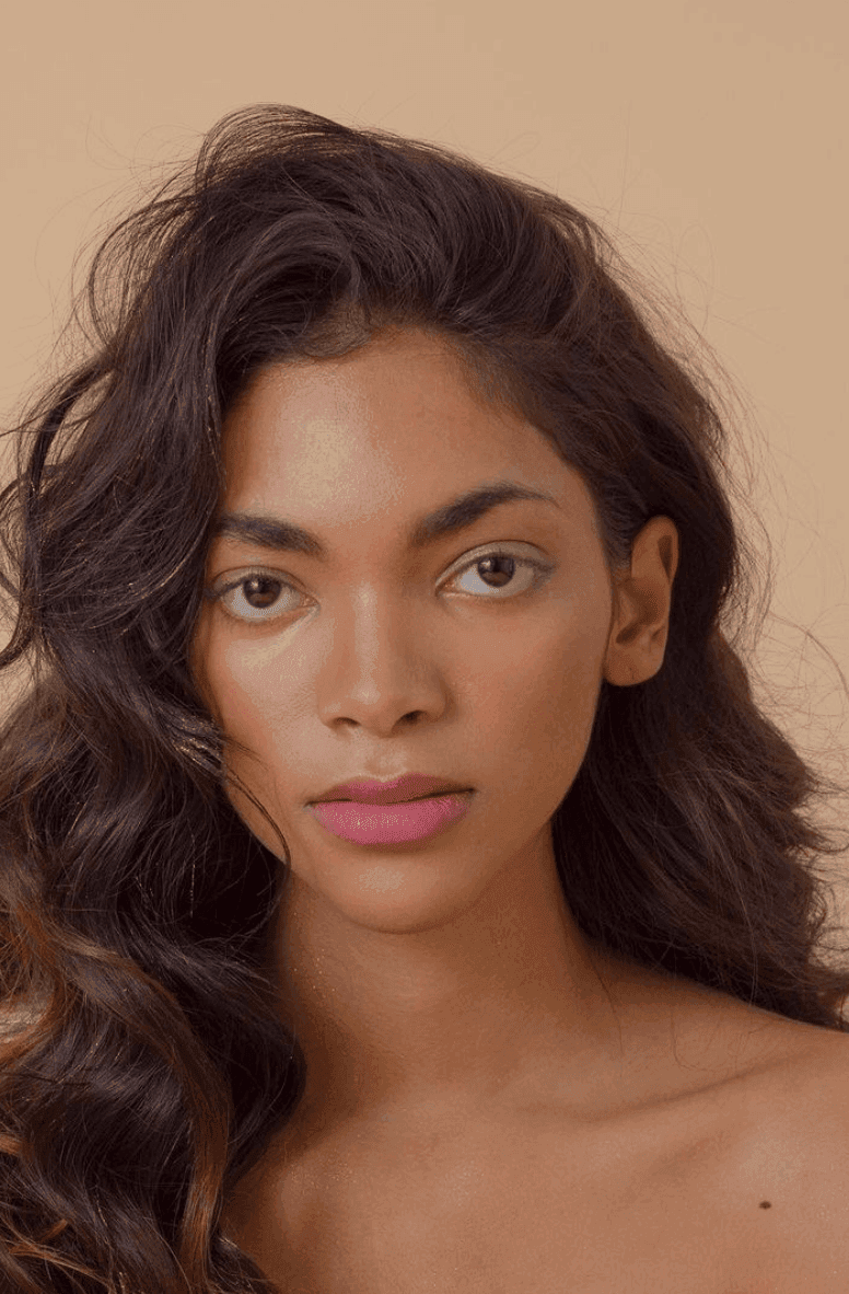 Portrait of a person with long wavy hair and pink lipstick against a neutral background.