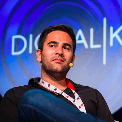 Man wearing a lanyard and microphone on stage during a digital conference.