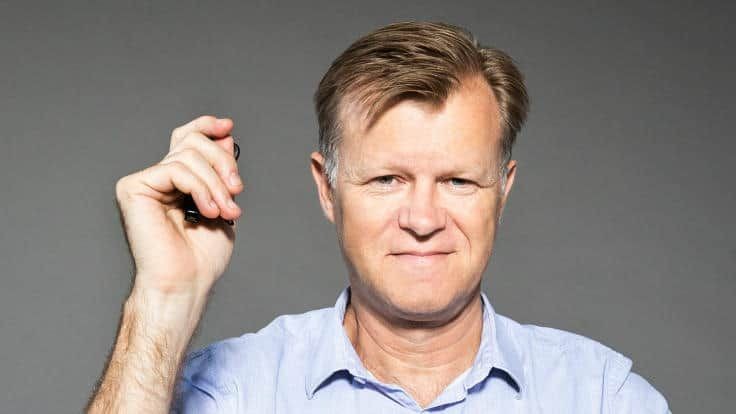 Man in a blue shirt holding a small object against a gray background.